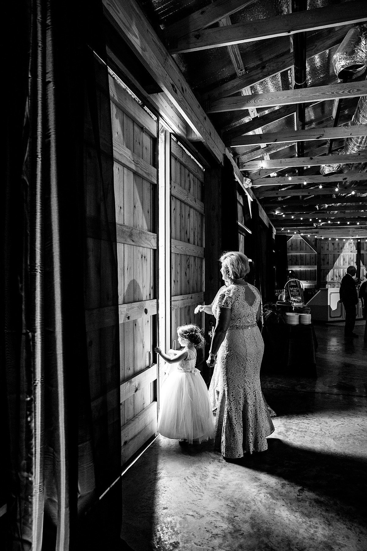 Black and white photo of the mother of the bride and flower girl sneaking a peek of guests arriving