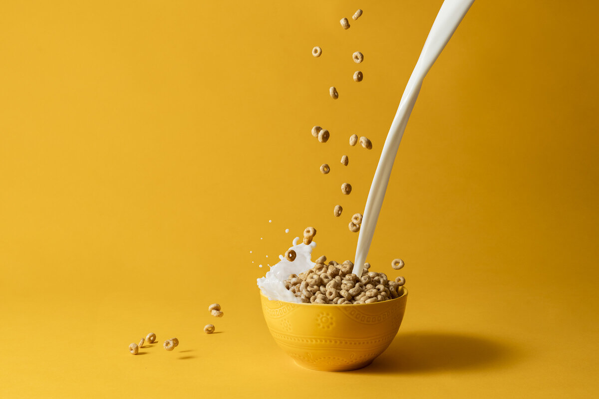 Cheerios cereal splashing out of a yellow bowl with milk on a yellow background.