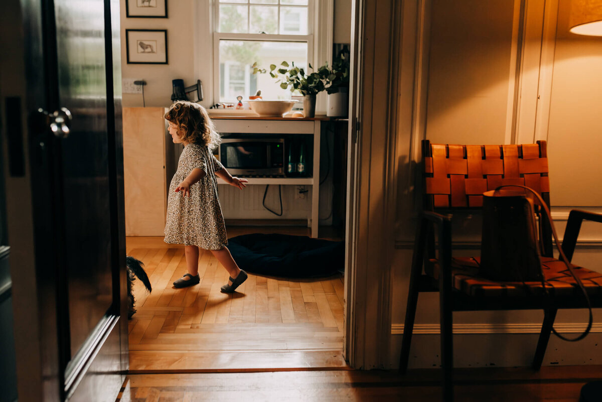 A young girl wearing a floral dress dances in a doorway in her kitchen
