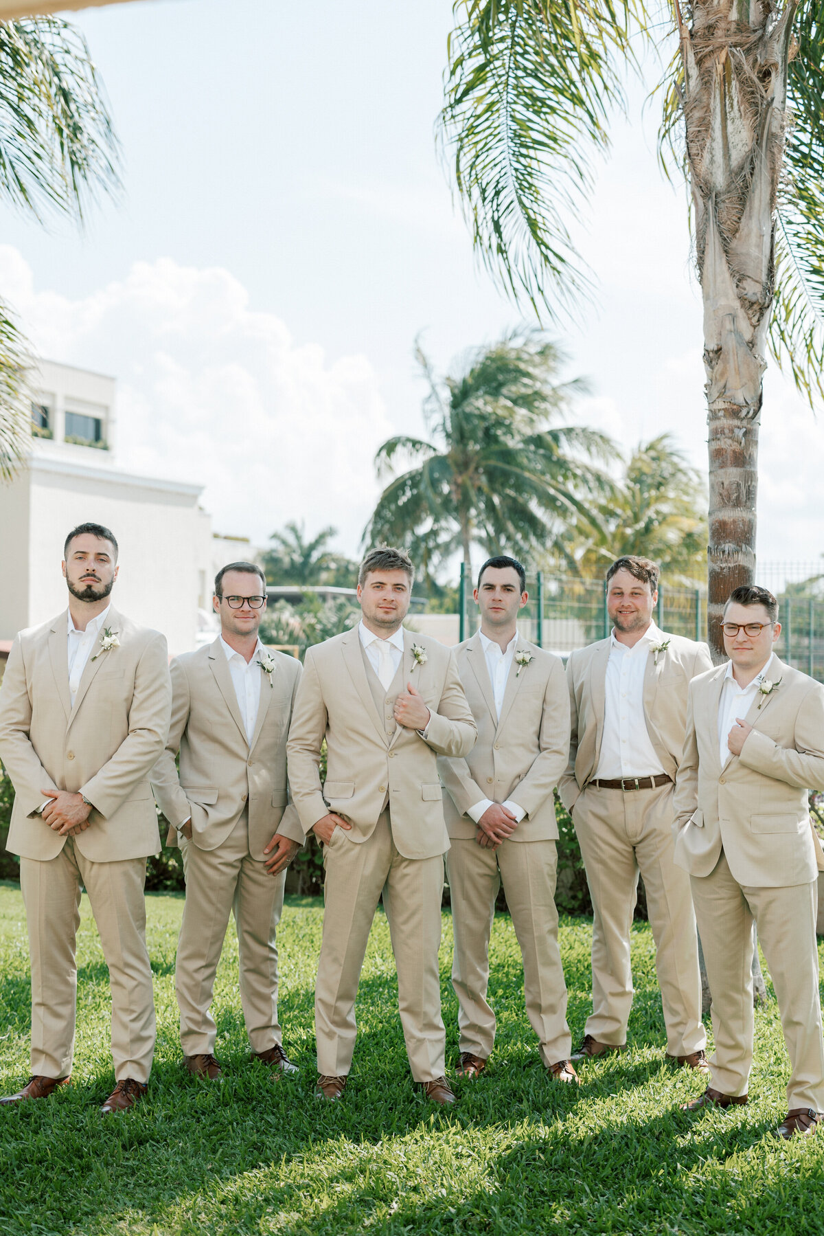 Groom and groomsmen in tan suits pose at sunny Cancun destination wedding.