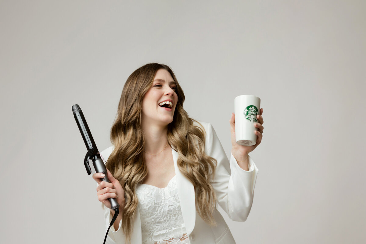 Trista stands with  hair dryer in one hand and Starbucks cup in the other.