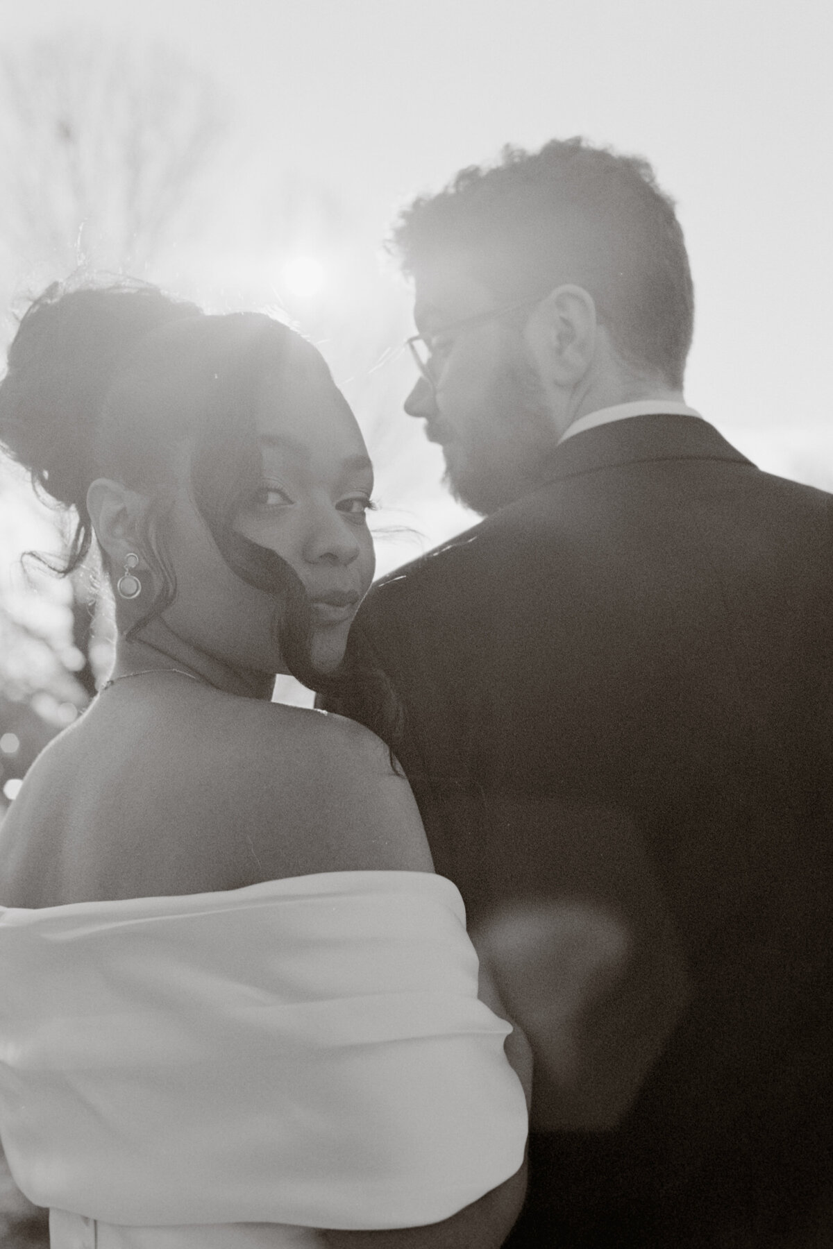 bride cuddles onto groom's shoulder as the sun shines through