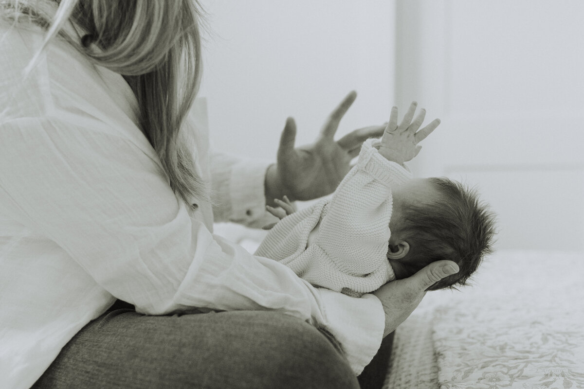 black and white photo of a mom holding her newborn baby and the baby is holding his hand up in the air, taken by a langley family photographer