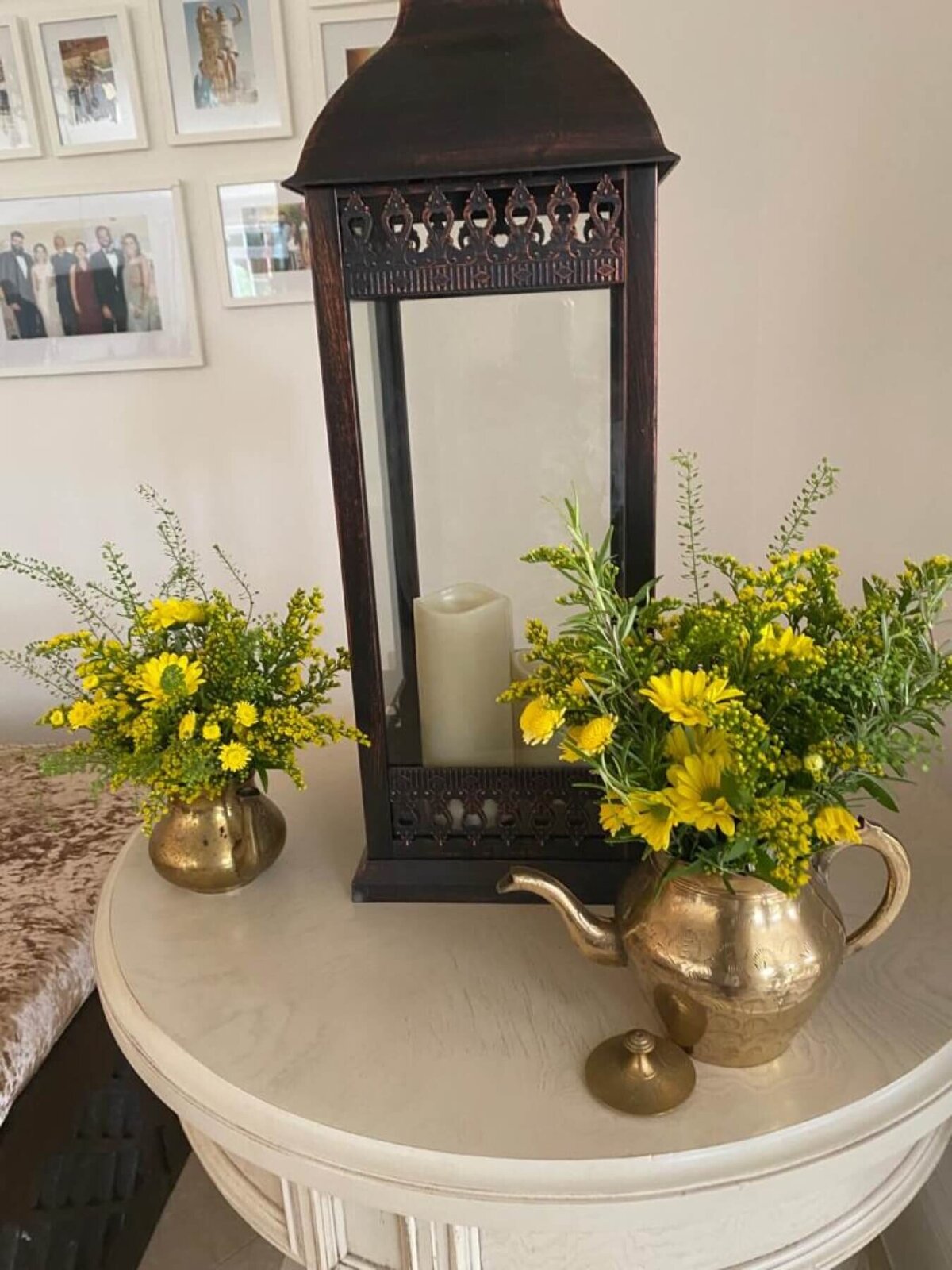 Large rustic lantern sat on a wood table with yellow garden flowers in rustic gold tea pot and vase