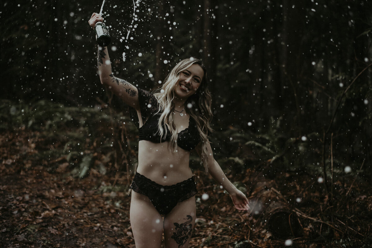 girl out in the forest in her lingerie, spraying champagne  in the air. She is more relaxed and smiling with her arms back in this one.