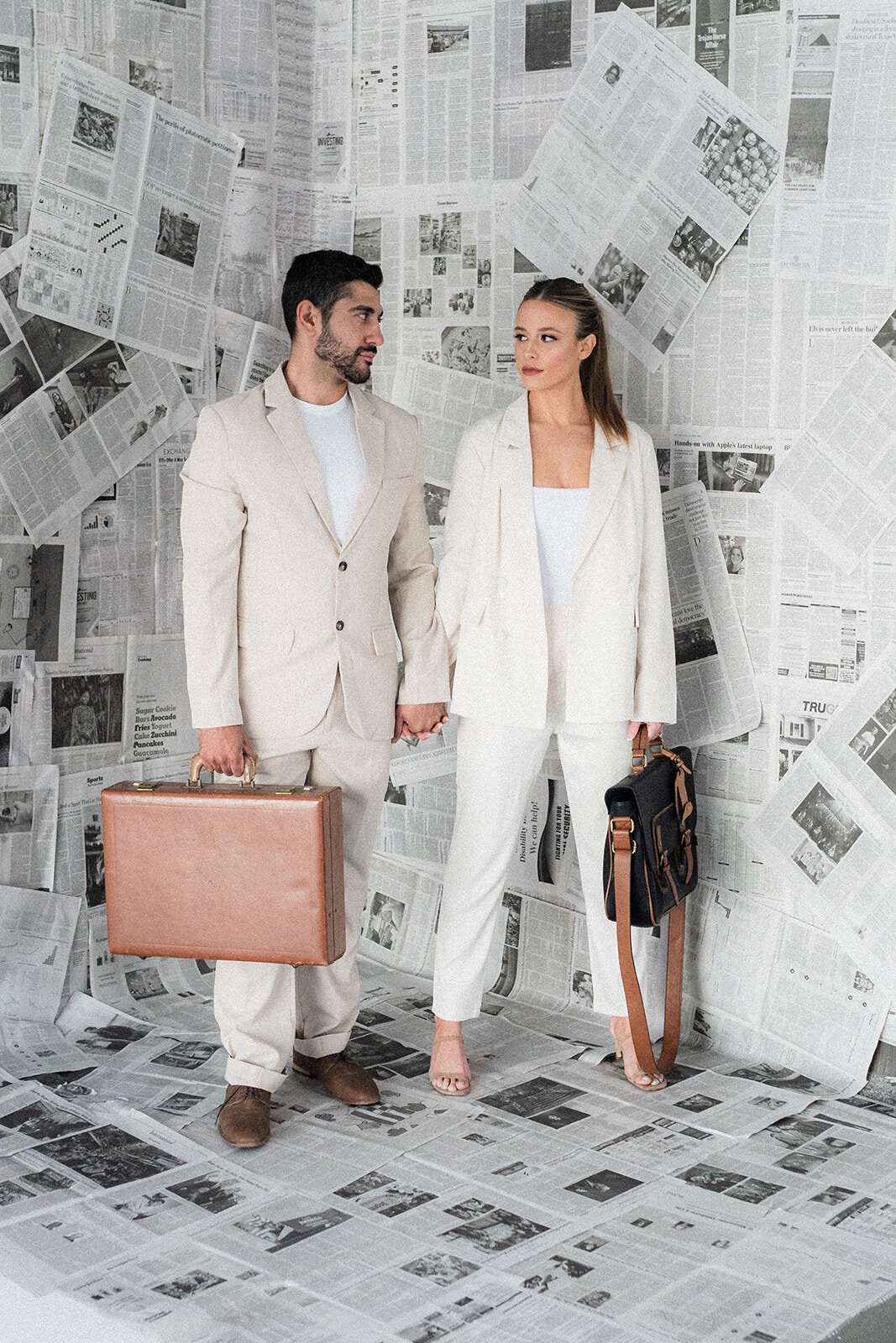A couple holds bags in front of a newspaper wall