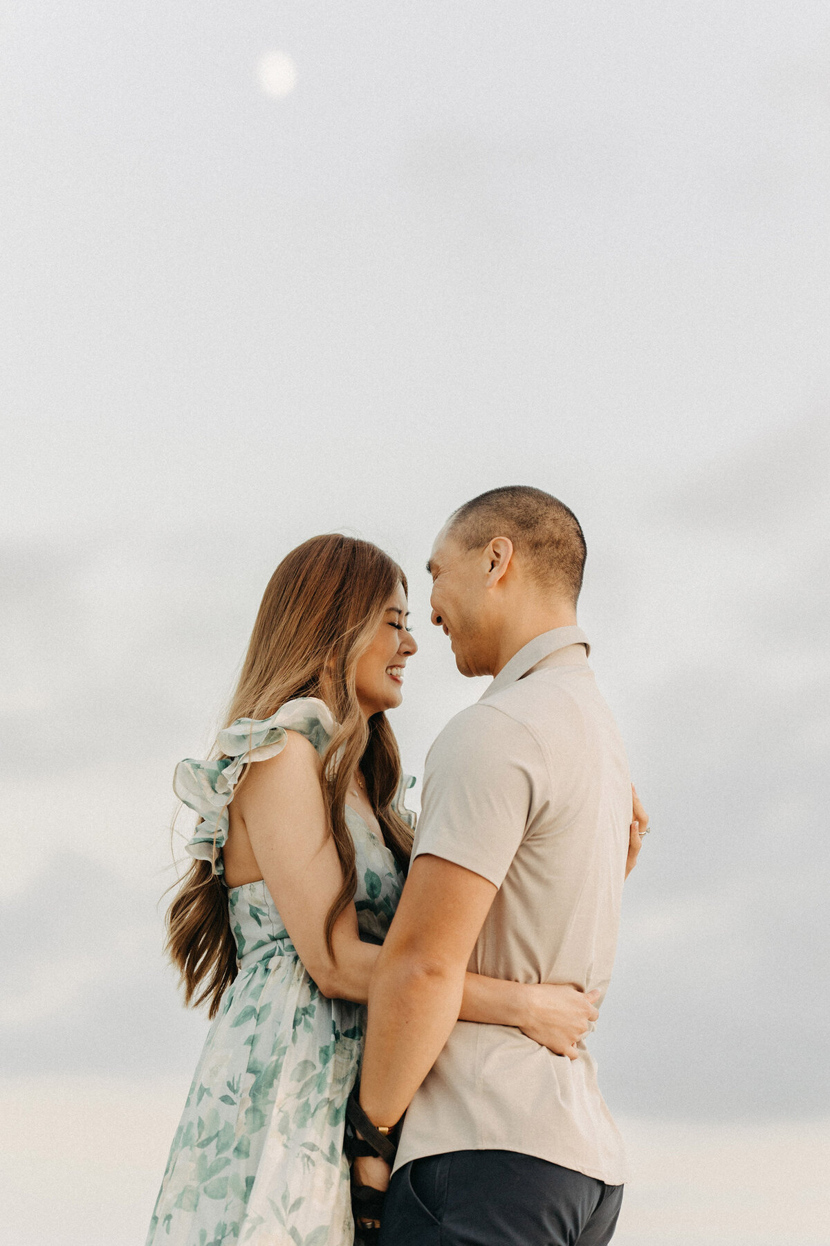 Couple smiling and holding each other under a soft evening sky at the beach in San Diego.