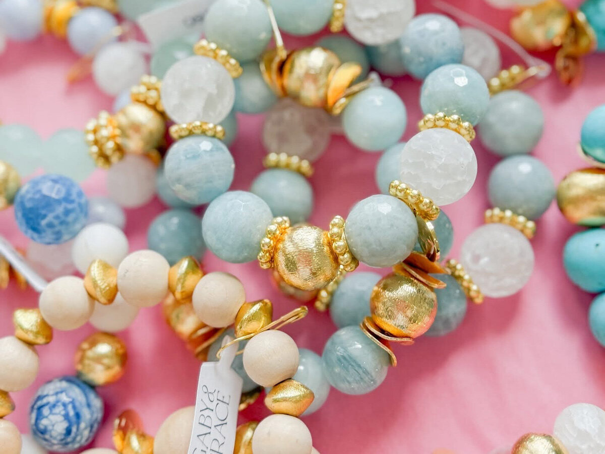 Assorted handmade gemstone and wood bead bracelets with gold accents in soft blues, whites, and pinks, part of Gaby & Grace’s seasonal collection.