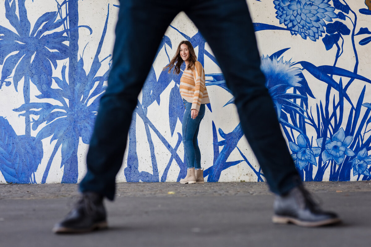 A women stand behind a man legs in front of a blue mural