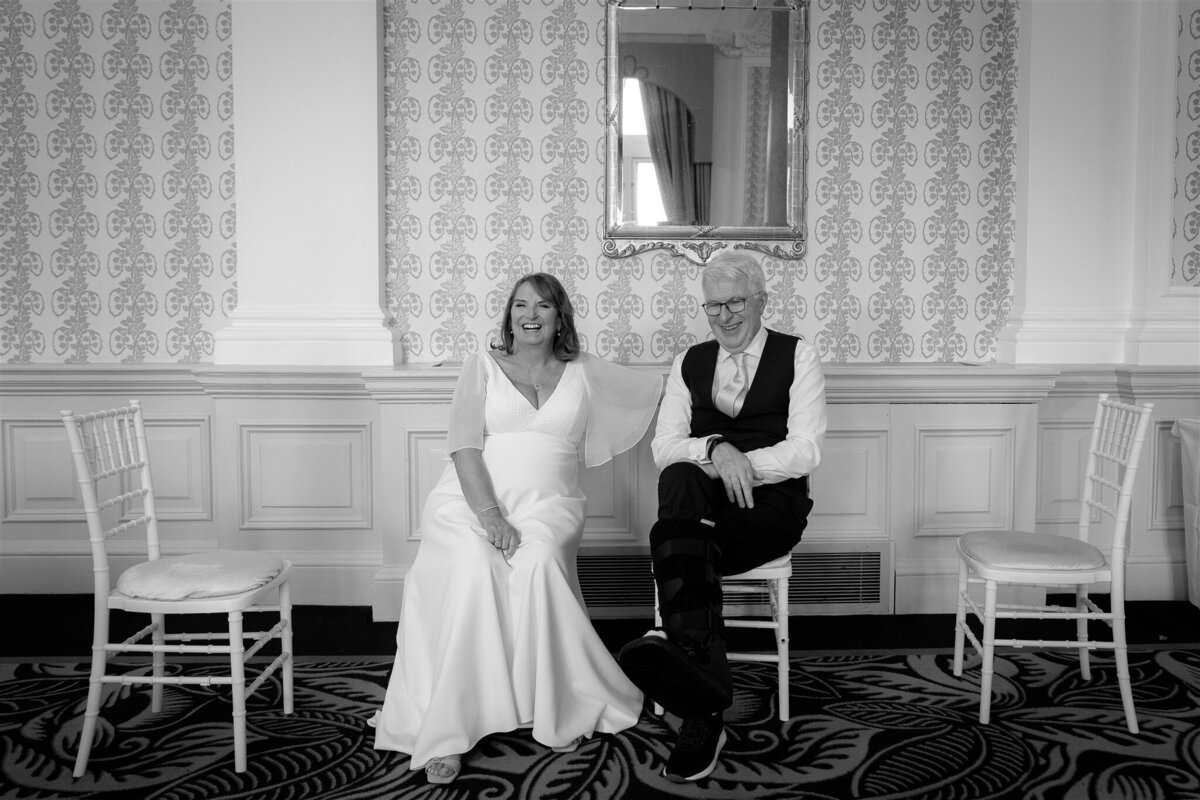 Hotel Balmoral Edinburgh wedding couple sit down to take a rest in two chairs amongst four.