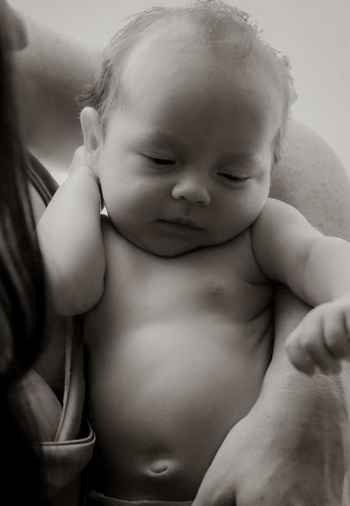 Black and white baby portrait, naked, in mom's arms during a lifestyle newborn session.