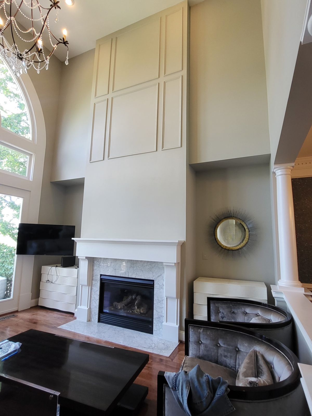 living room with fireplace with white mantle surrounding white veined with grey veins marble and nooks with bureaus two tufted barrell oversized chairs, overly large coffee table in black lacquer in front of the sofa