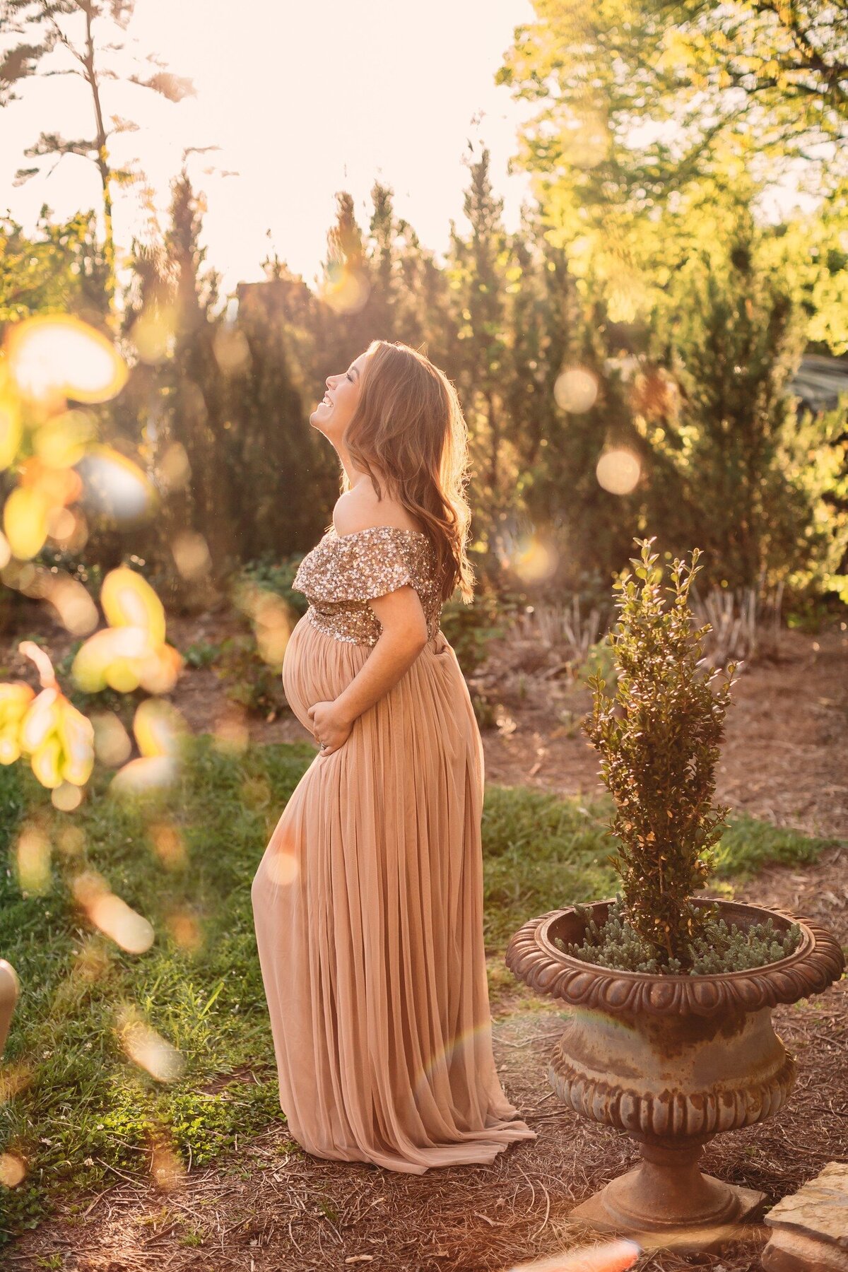a pregnant woman looking up at the sky joyfully as the sun shines on her