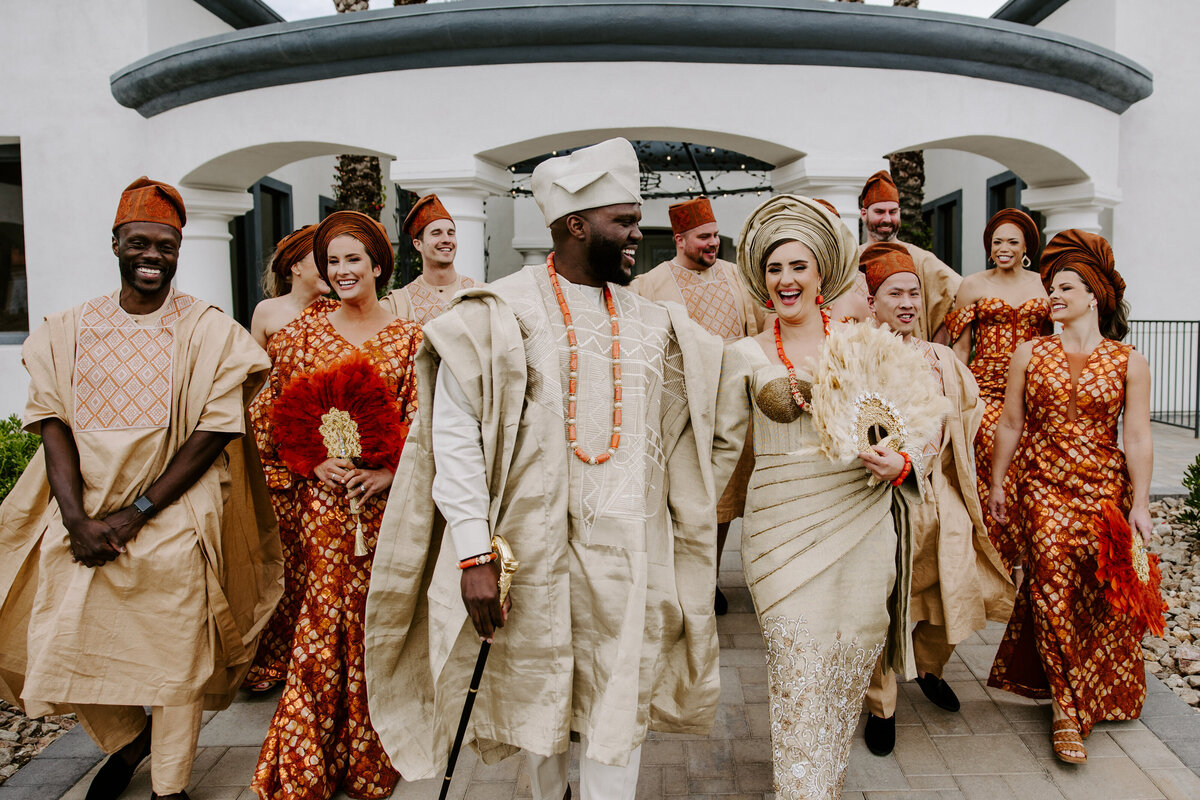 A couple walks on their wedding day with their family smiling around them.