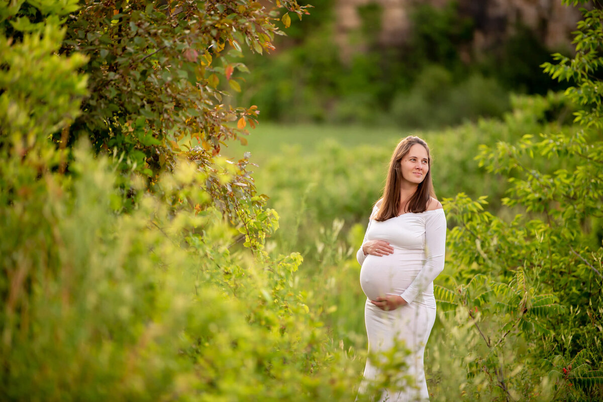 pregnant woman in a field wearing a white dress cradling her belly 
