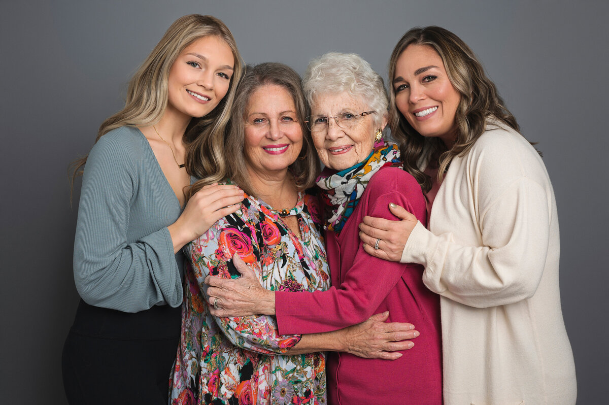 Four generations of women posing together, smiling and hugging by Leslie Q Photography