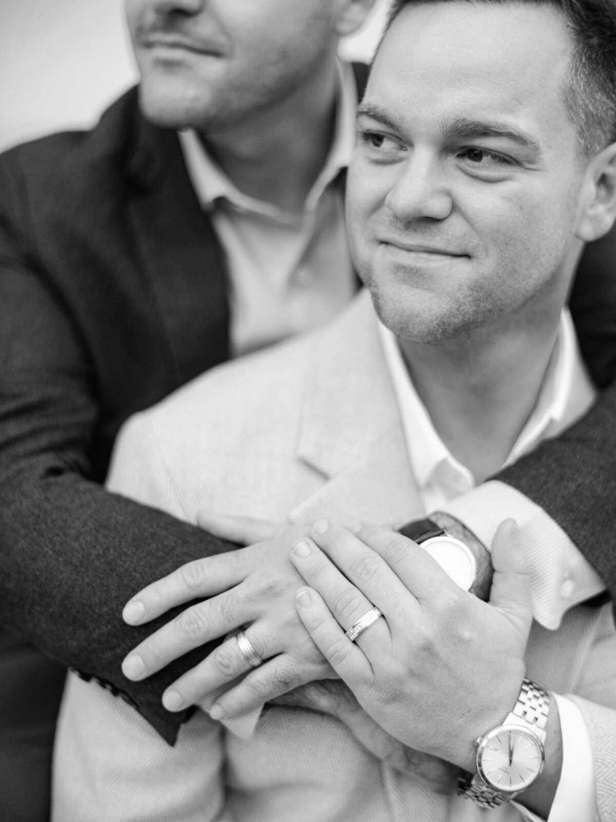 A captivating close-up where one partner embraces the other from behind, showcasing tenderness and love while highlighting their wedding bands in a beautifully intimate moment.