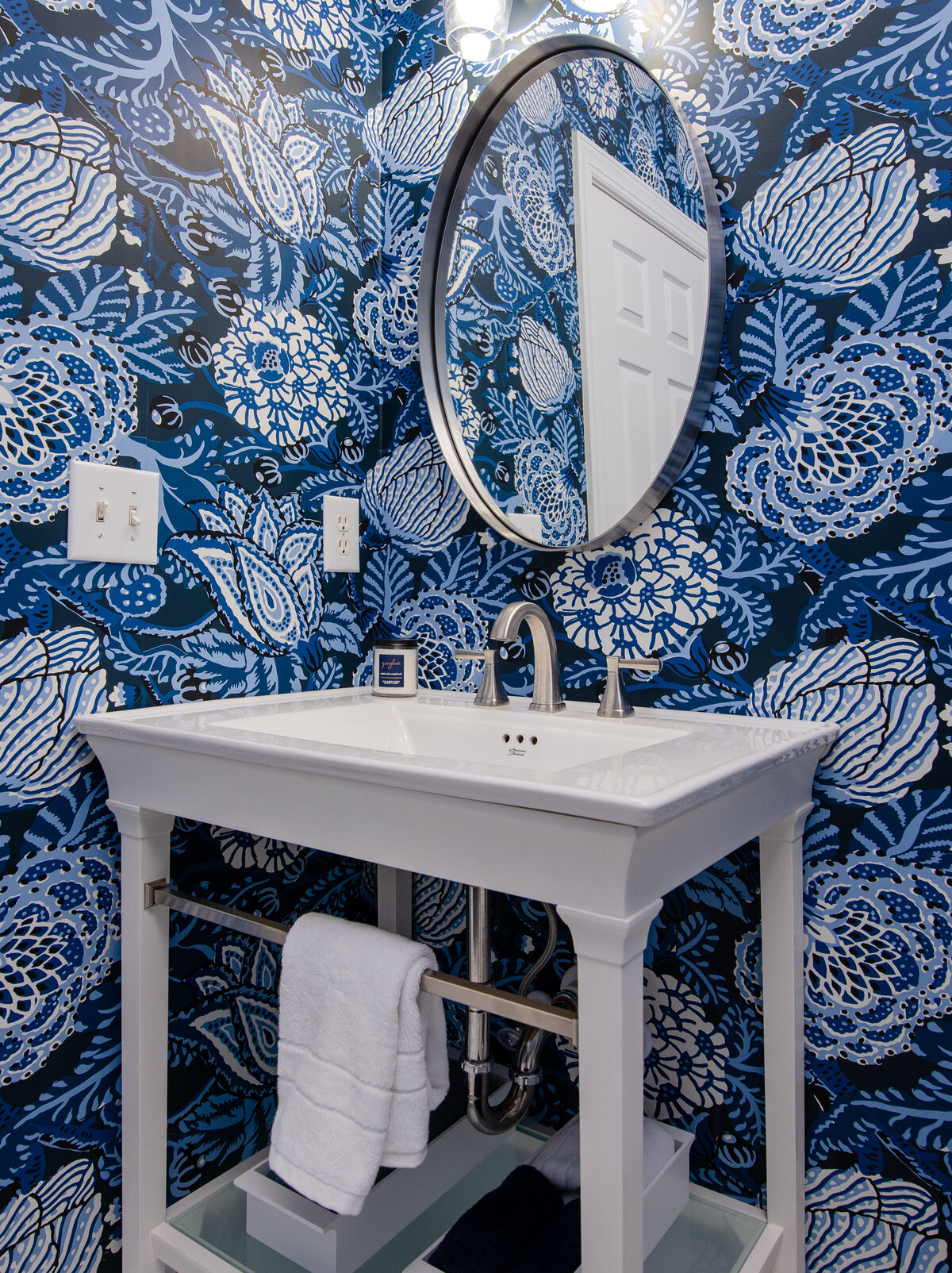 Bold bathroom in Lake Norman, NC, with blue patterned wallpaper and a classic white pedestal sink.