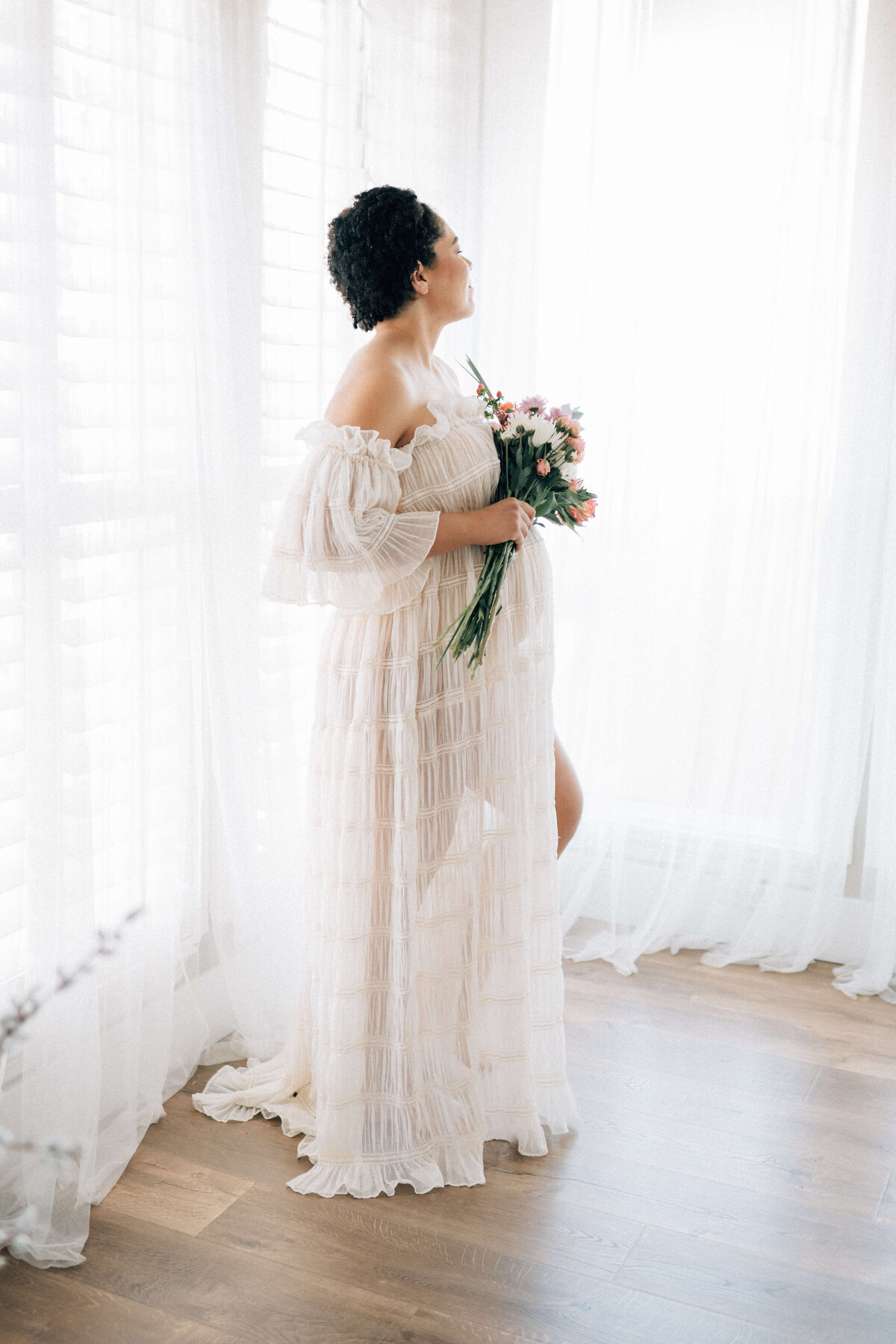 pregnant mother holding flowers while looking out a window