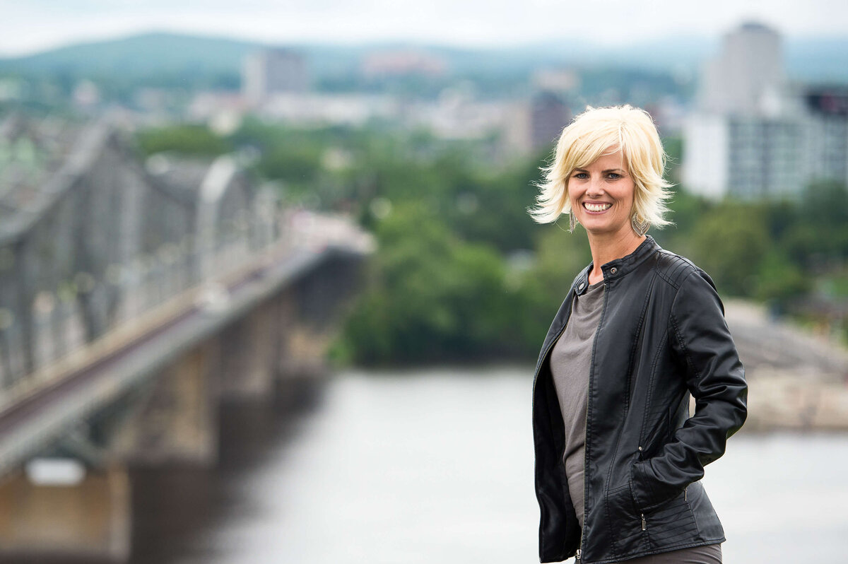 Ottawa brand photos of a blonde-haired woman wearing a black leather jacket with the Ottawa River and canal in the background.  Captured outdoors by JEMMAN Photography COMMERCIAL