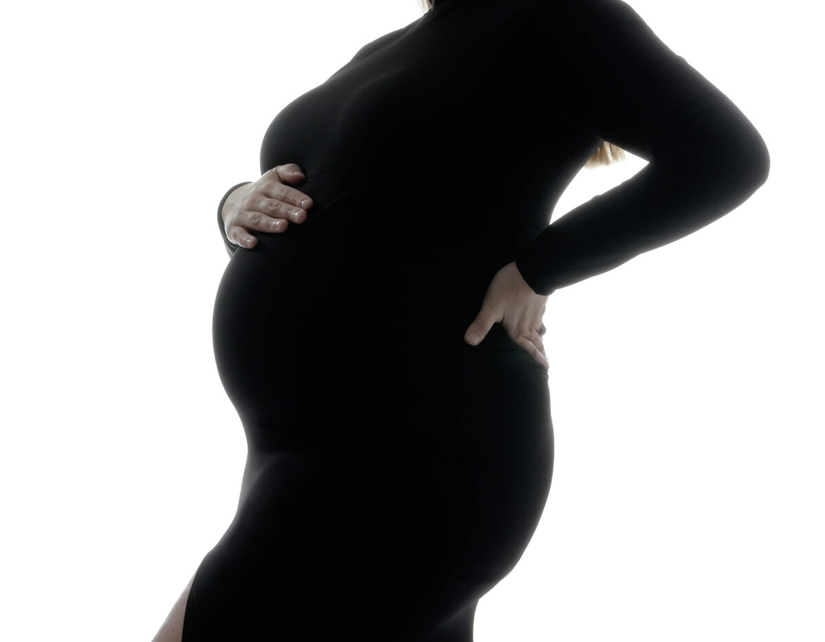 Close up view of mom-to-be baby bump in a fitted long sleeve black dress.