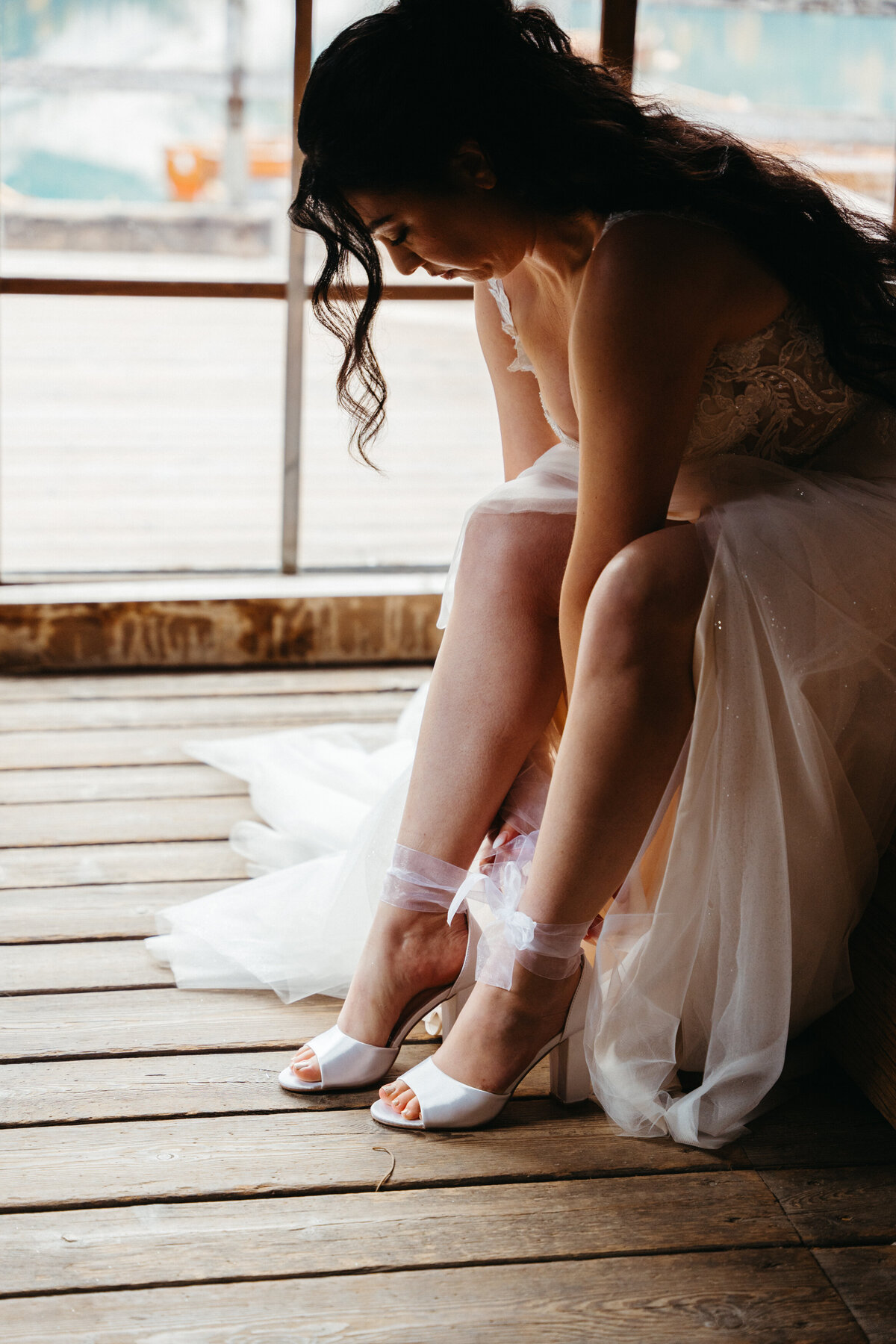 Bride adjusting heels on wooden floor before ceremony