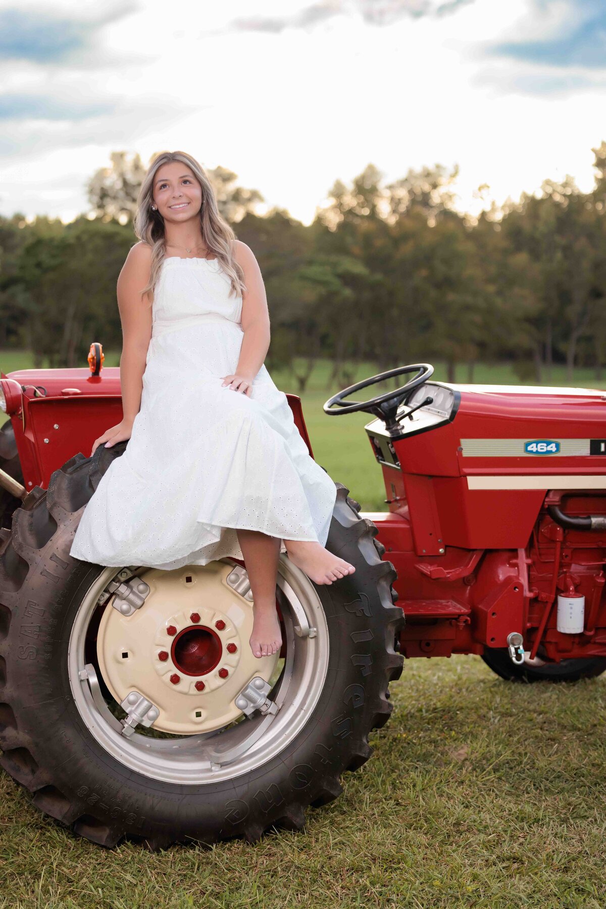 Raleigh senior wearing white dress sitting on a tractor for senior pictures.