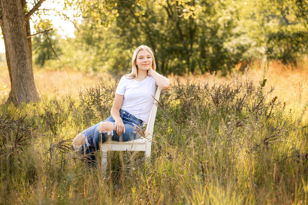 Senior girl posed in white chair sitting in wildflowers.