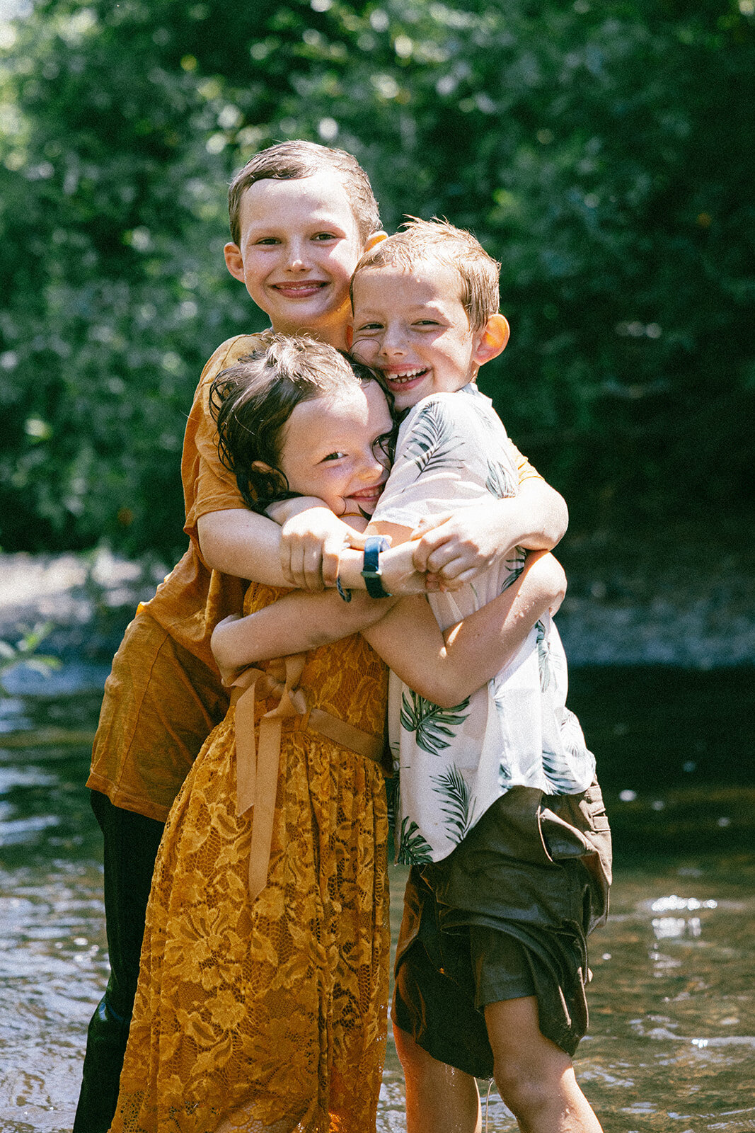Kids hug each other for family photos while bathed in sunlight in a river in Oregon. 