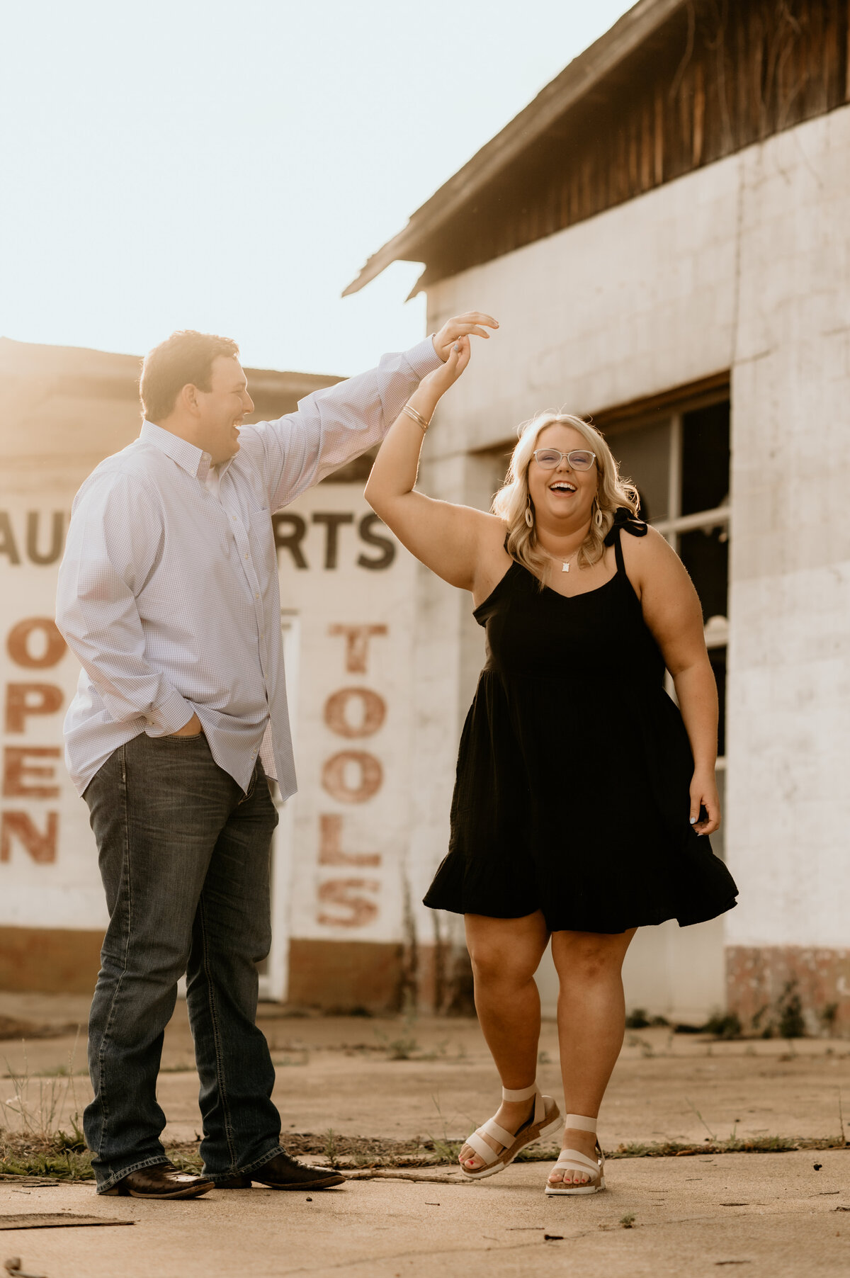 downtown little rock engagement session with man twirling his fiance as they dance on the sidewalk as the sun sets in the distance