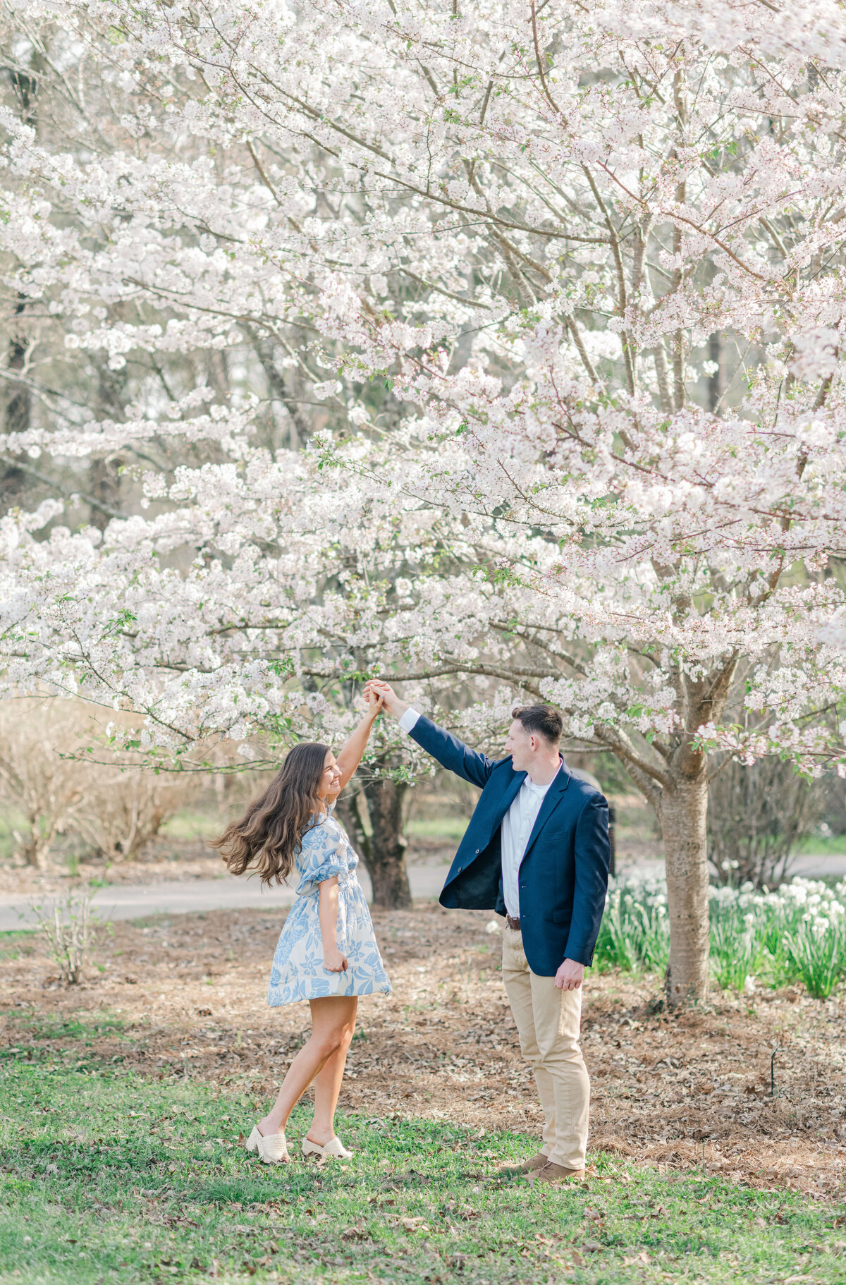 Man holding womans hand while she spins in a field of cherry blossom tress wearing blue