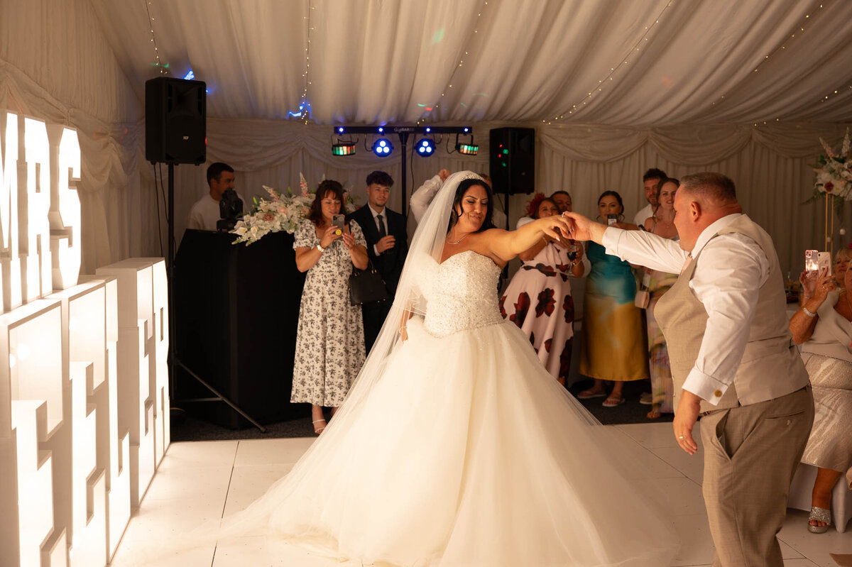Bride twirling on dance floor during wedding reception – Mr & Mrs Sign backdrop.