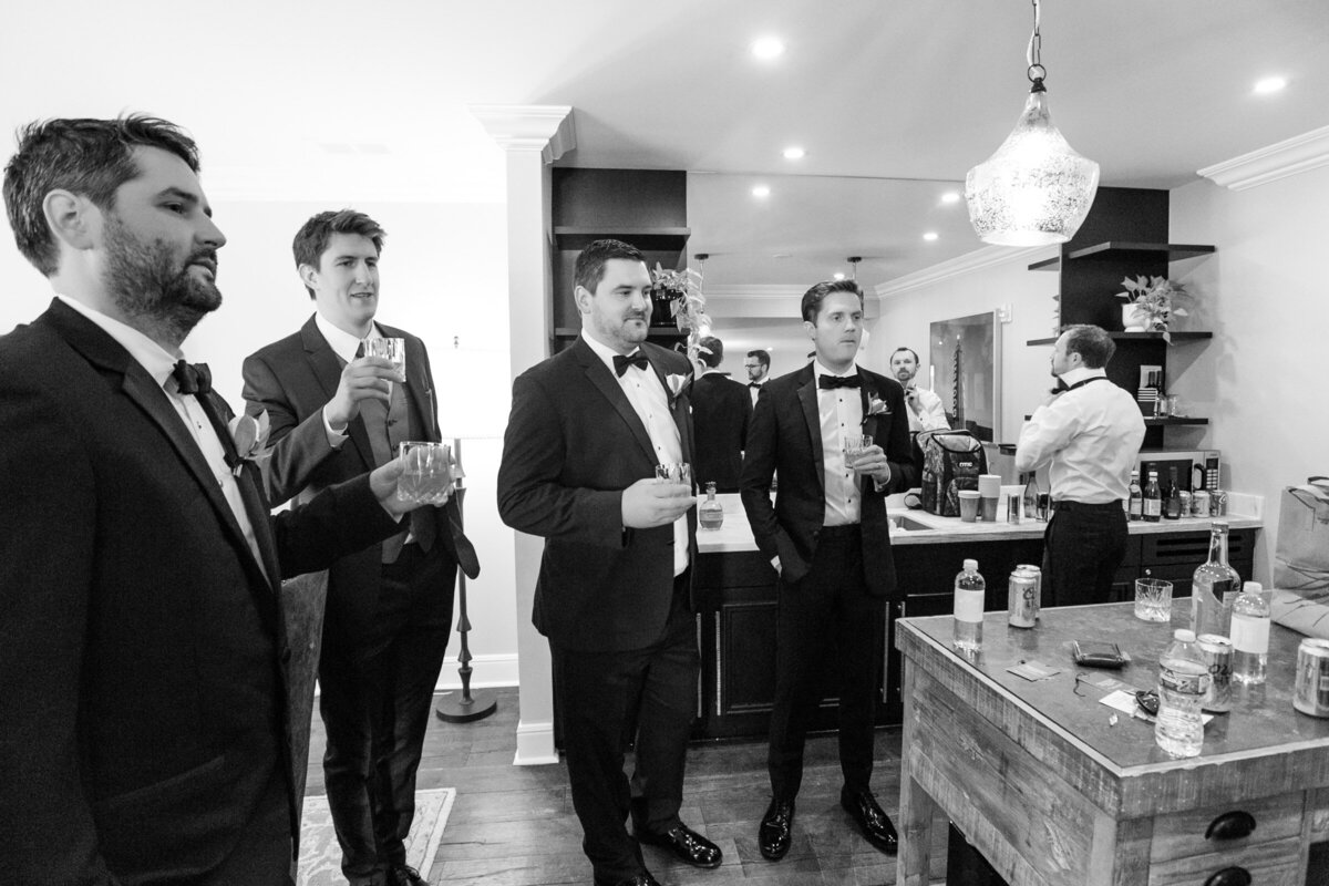 black and white candid of the groom and groomsmen toasting before the ceremony at The Adolphus in Dallas, capturing a classic and celebratory pre-wedding moment.