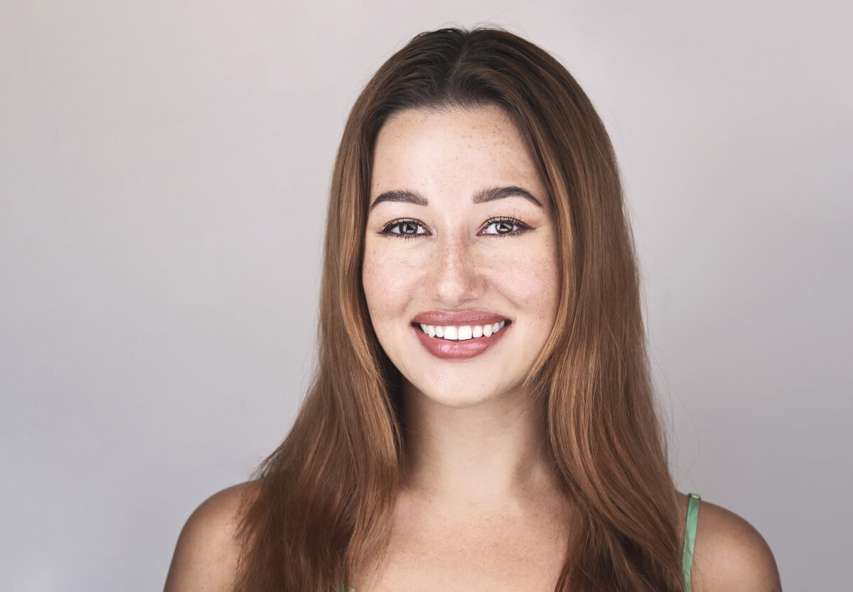 Woman with long brown hair and a green tank top poses for a studio headshot. She is looking at the camera and smiling. Philadelphia and Main Line Headshot Photographer.