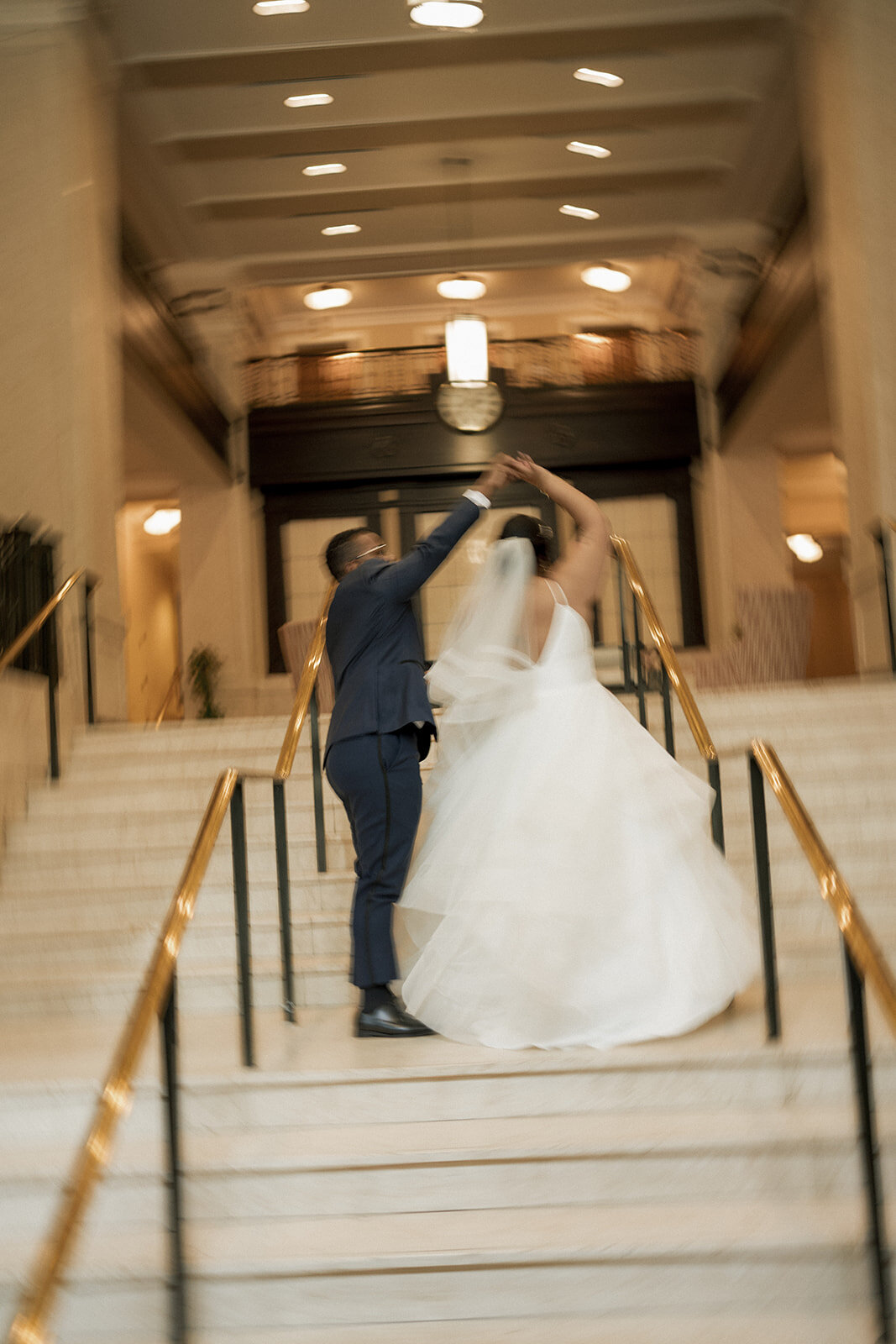spinning spouse in dress on stairs on wedding day in ballroom venue