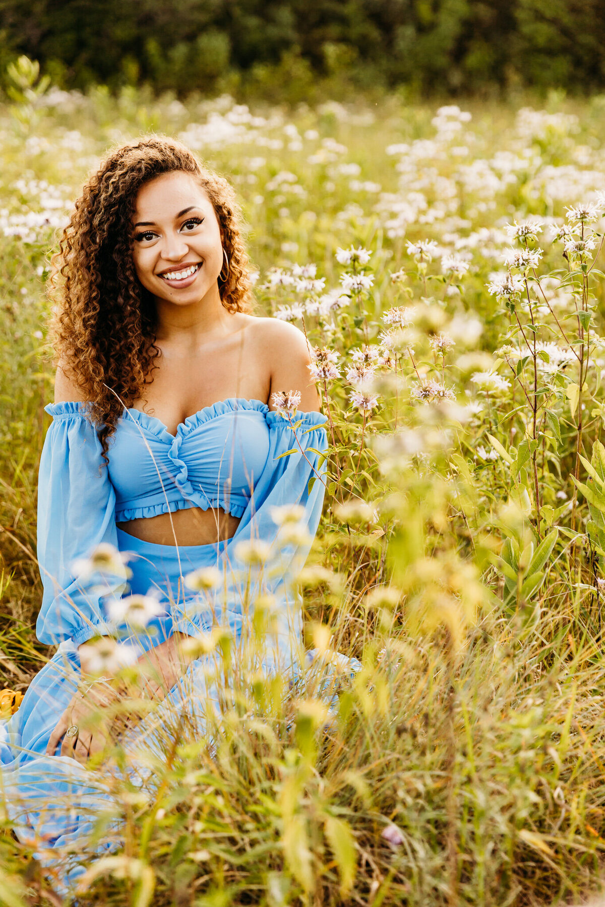 beautiful young woman with curly hair smiling while sitting in a field of bee balm in Oshkosh