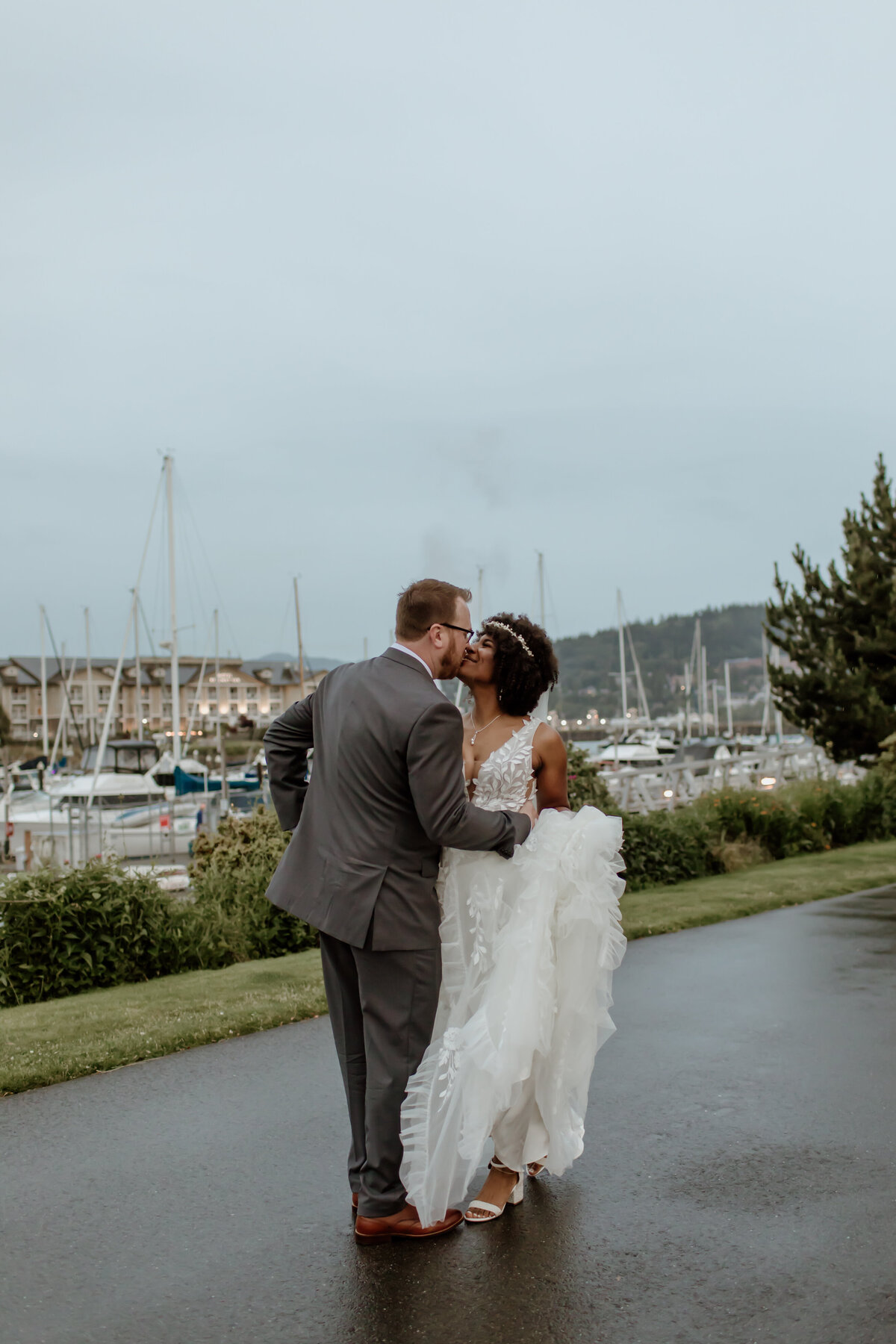 A just married couple kisses in the rain with the Bellingham waterfront in the background. Captured by Fort Worth Wedding Photographer, Megan Christine Studio