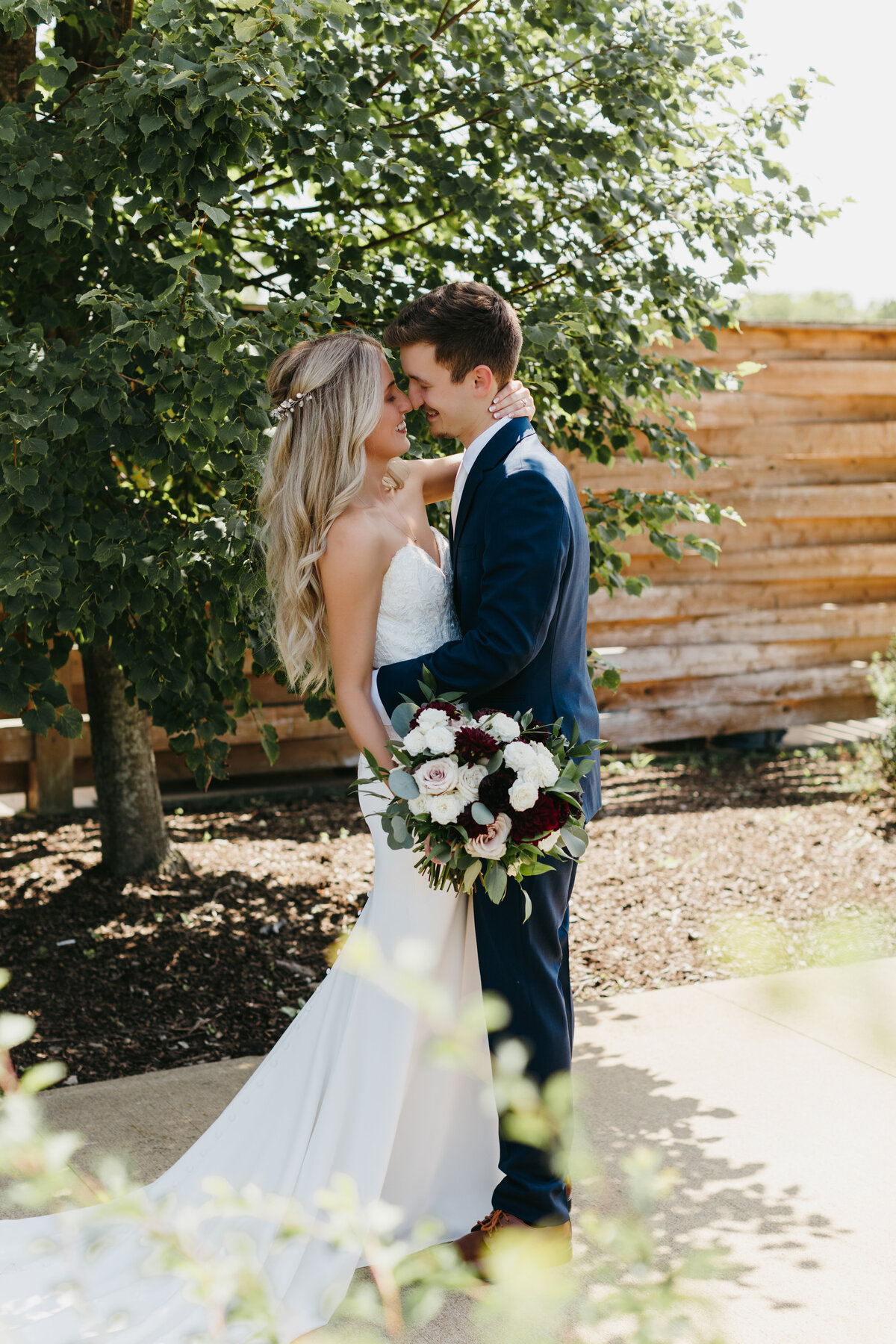 Bride and groom with their heads together standing under a green tree