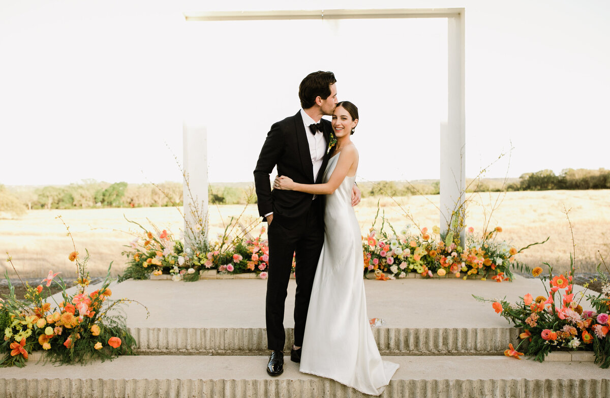 Bride and groom standing in front of colorful florals at Propect House Wedding, Austin