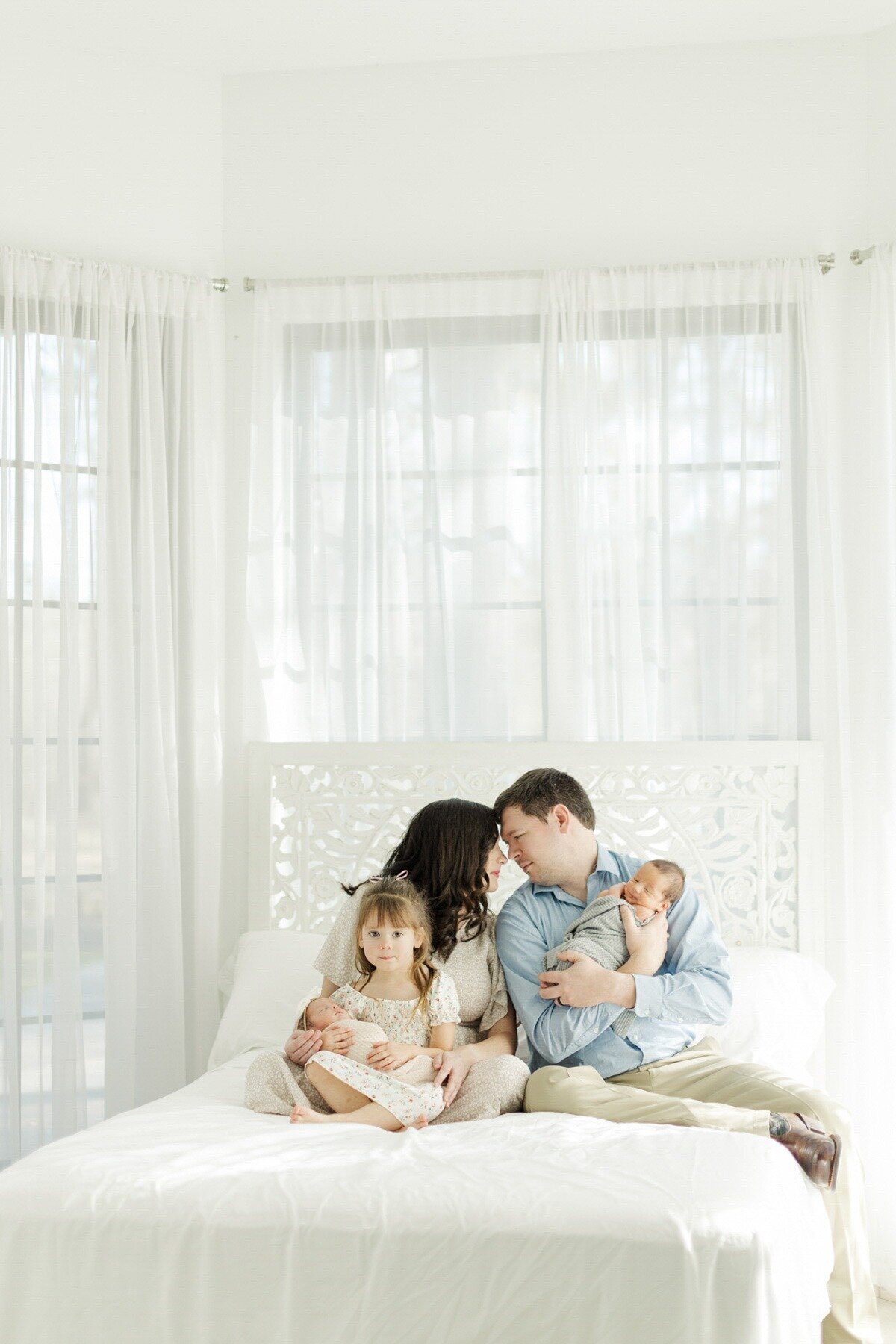 family of five snuggle on white studio bed together holding newborn twins