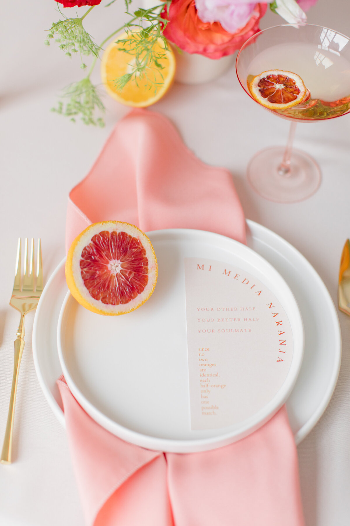 Place setting with pink napkin , blood orange and a menu on a white plate