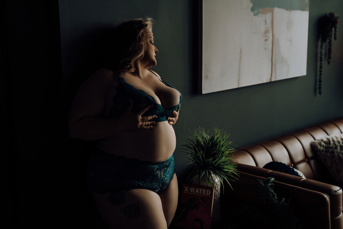 Dark boudoir portrait of woman in teal lingerie posing against wall of living room