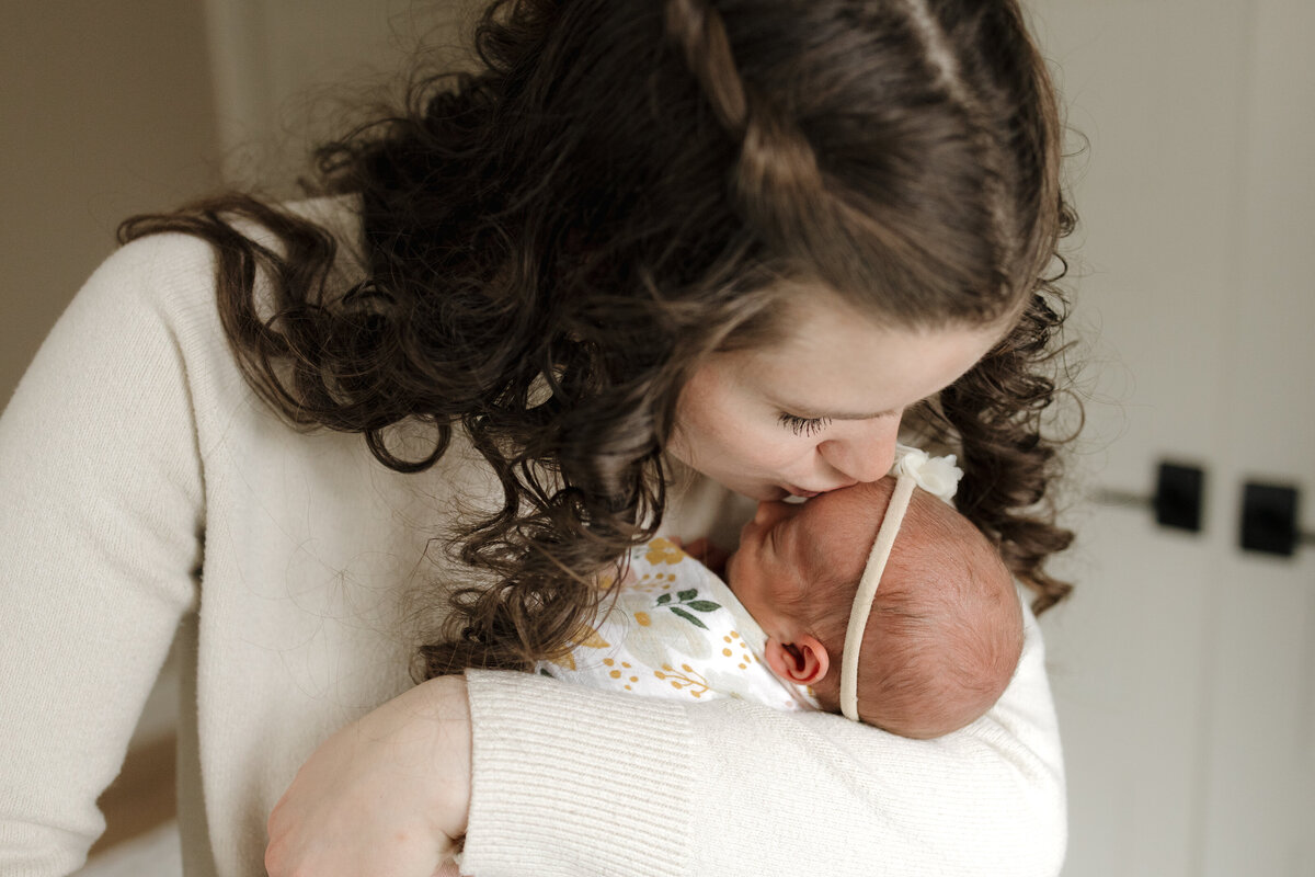 Longmont mom kissing newborn babys forehead while holding her