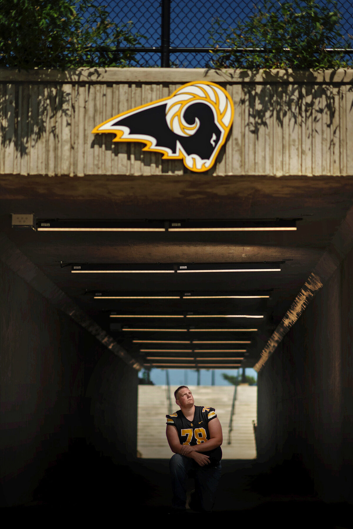 A high school football player kneels under his stadium's logo looking up to it