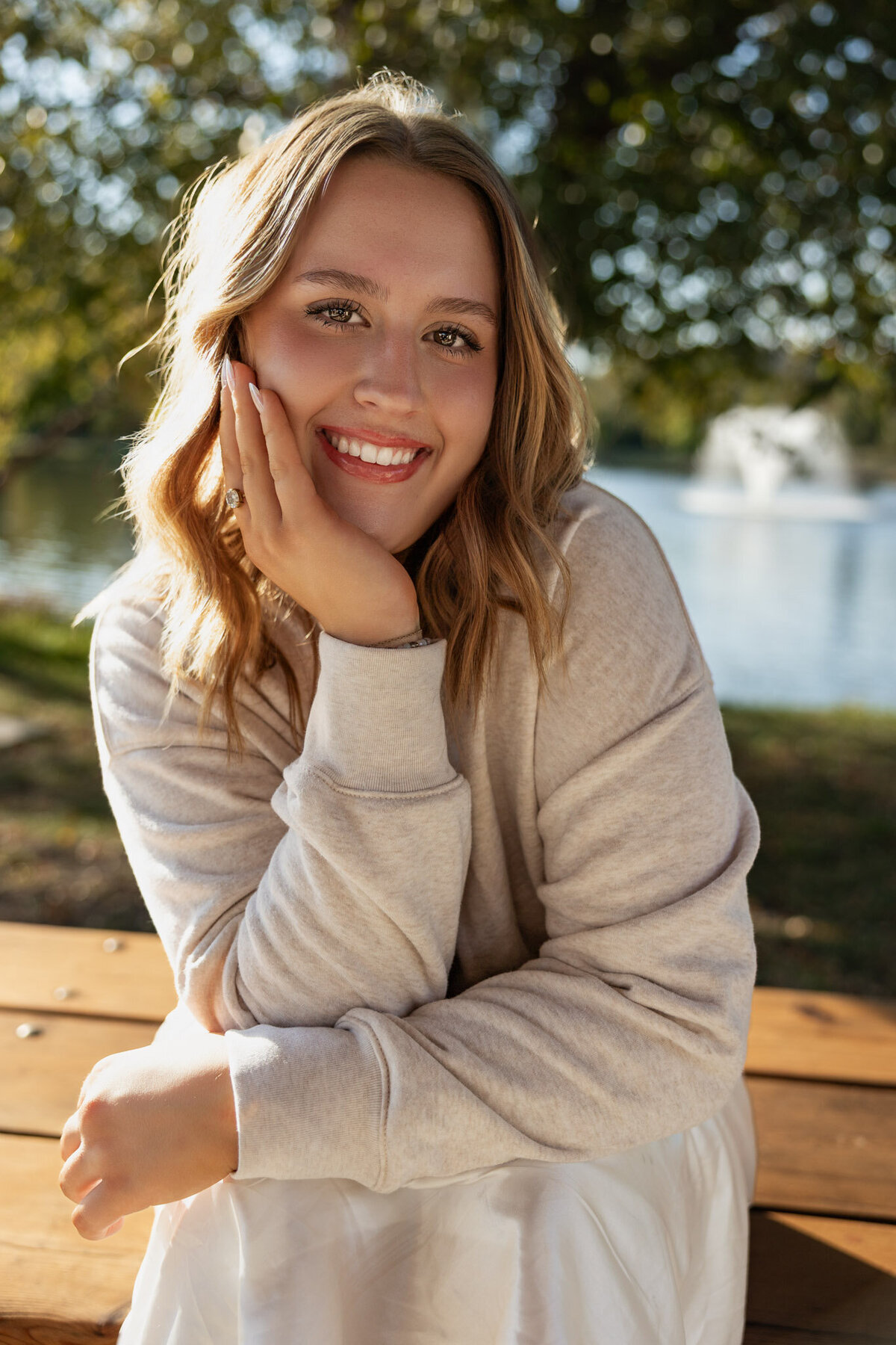 Senior girl sitting outdoors in cozy sweater smiling at camera in Lawrence KS