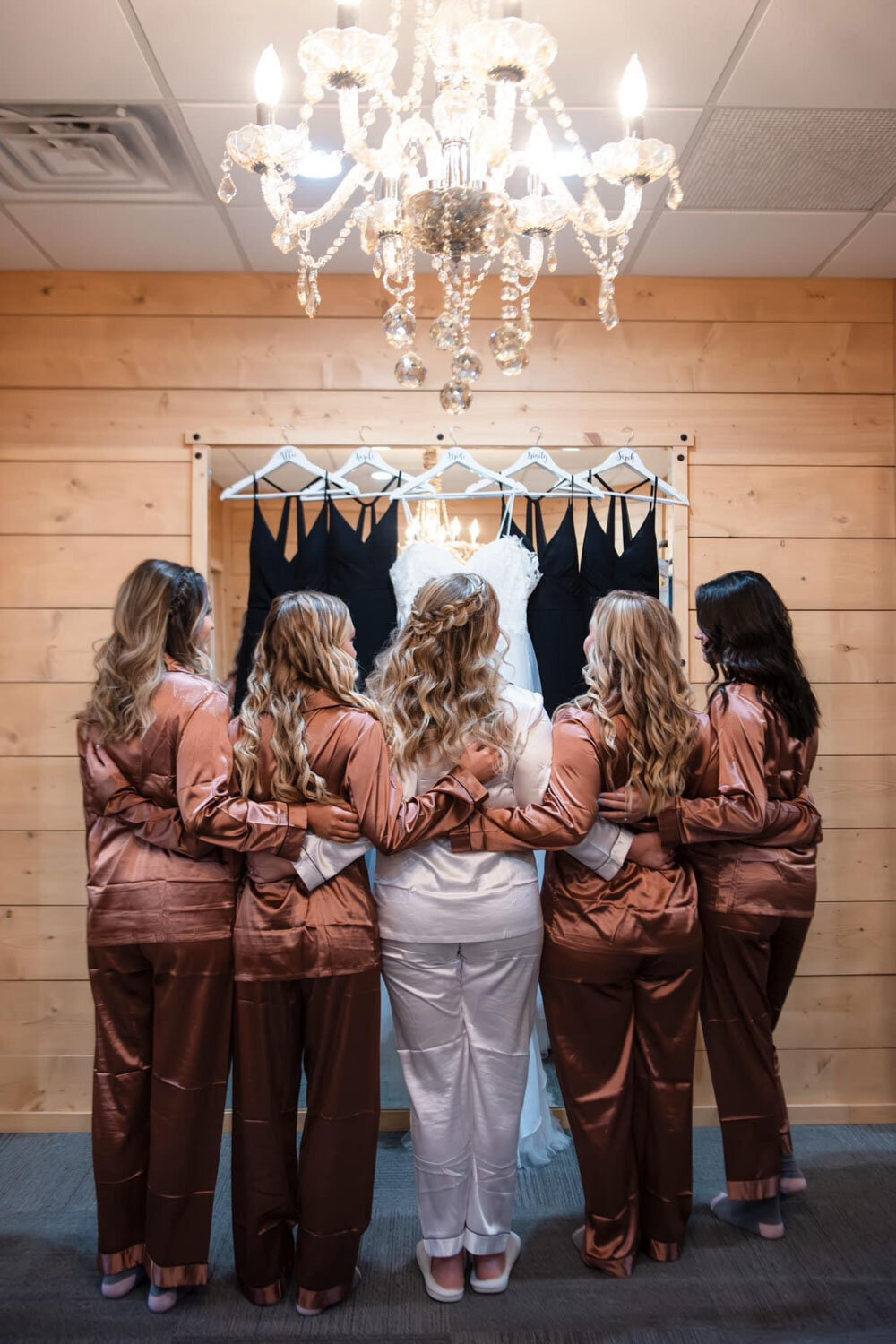 Bridesmaids in matching satin pajamas standing in front of dresses on hangers