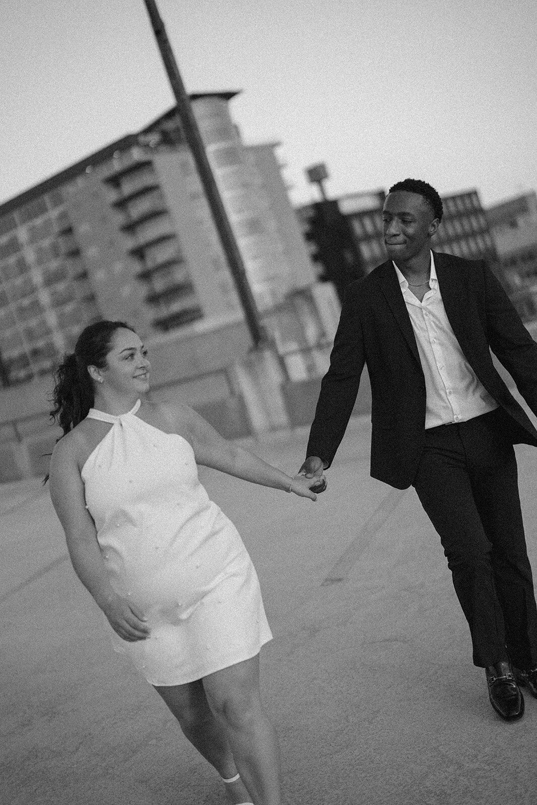 Black and white photo of engaged couple walking hand in hand on downtown Kalamazoo rooftop.