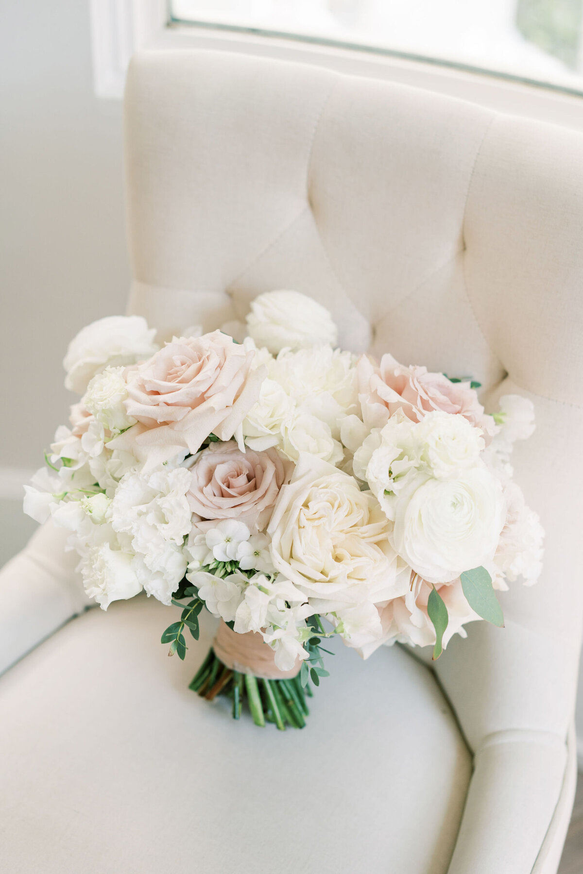 A bouquet of white and pale pink flowers rests on a beige upholstered chair, creating a perfect setting for a modern &amp; romantic wedding in Calgary.