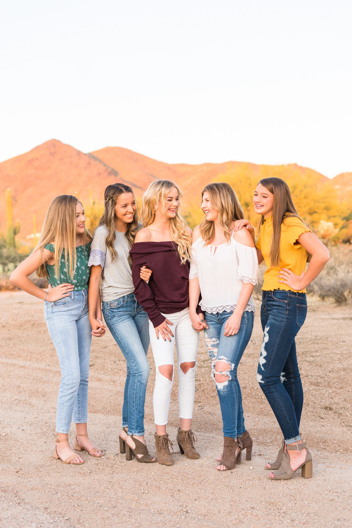 Five girls holding hands and laughing in desert