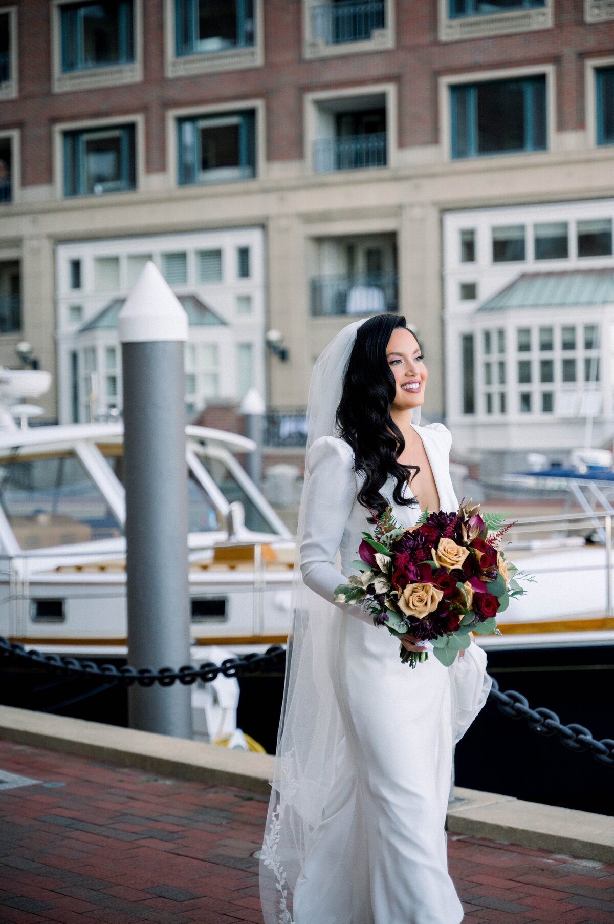 a bride walking in a wedding dress holding a flower bouquet with boats in the background